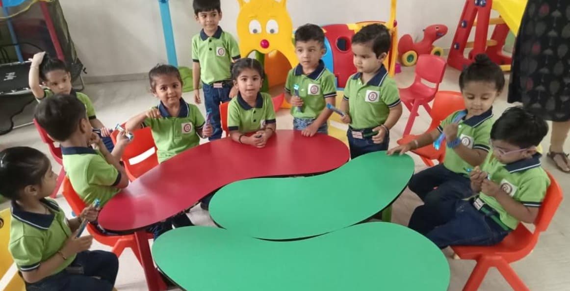 Children seated around colourful tables in a classroom with a slide, play house and other play equipment