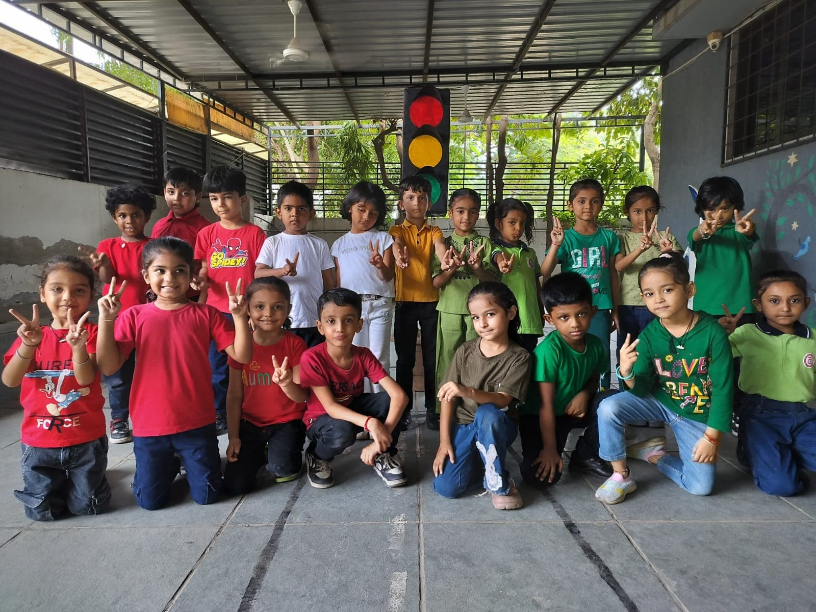 Children dressed in red, yellow and green making peace signs beside a model traffic light