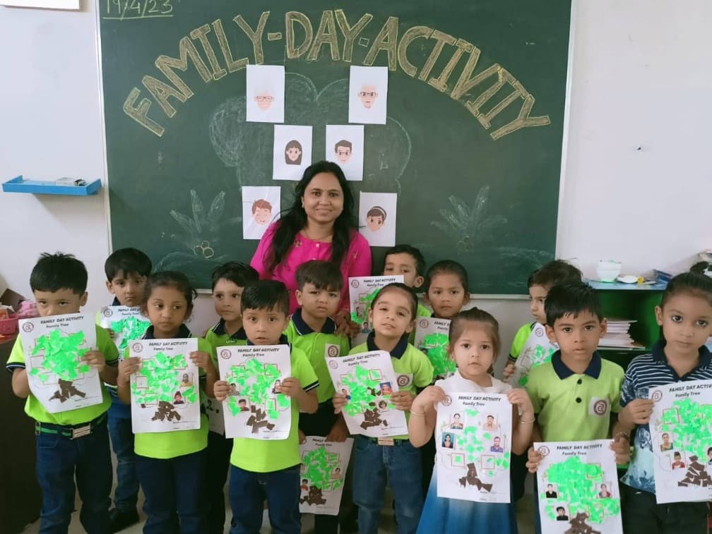 A teacher and children in uniform holding up their family tree crafts in front of a Family Day Activity chalkboard