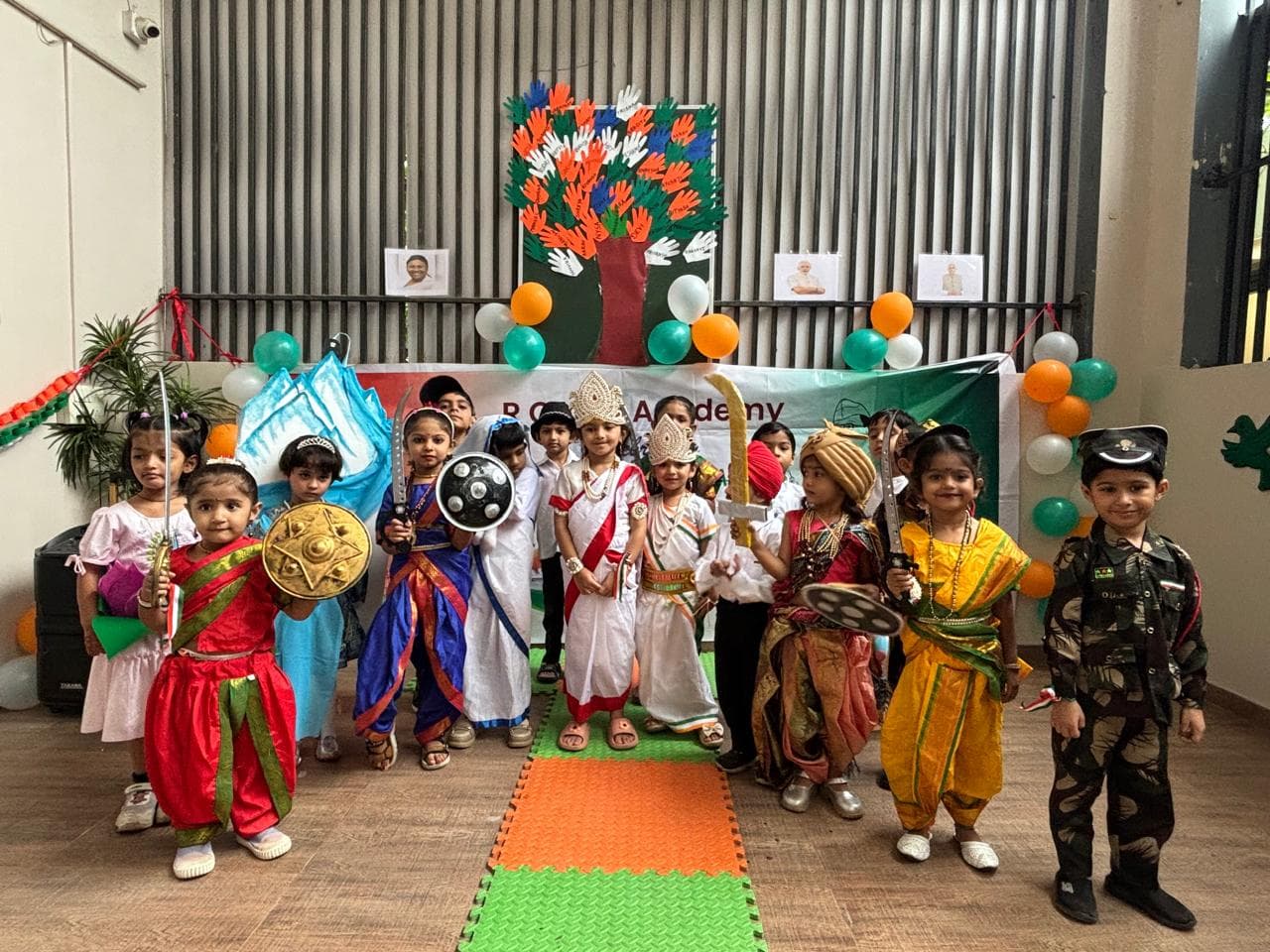 Children in fancy dress costumes in front of tricolour balloons and a handprint tree