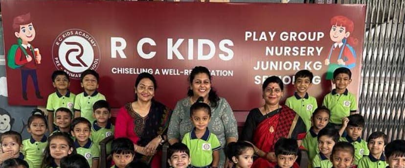 Teachers and children in uniform in front of the RC Kids signboard
